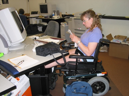 Photo of student working at an accessible computer workstation. Student is in a wheelchair. The workstation is adjustable and accomodates diverse access.