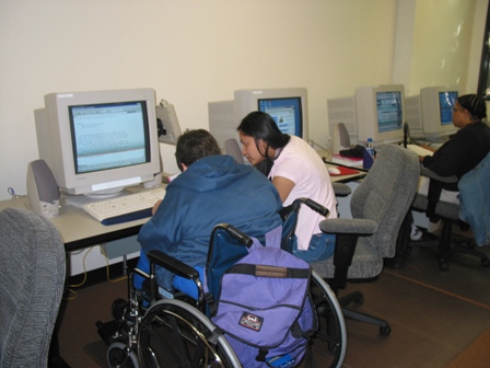 Photo of a student getting help from a classroom aide during a computer class. 